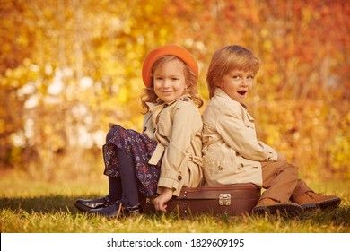 Deux enfants en trench-coat d'automne assis dos à dos dans un parc.